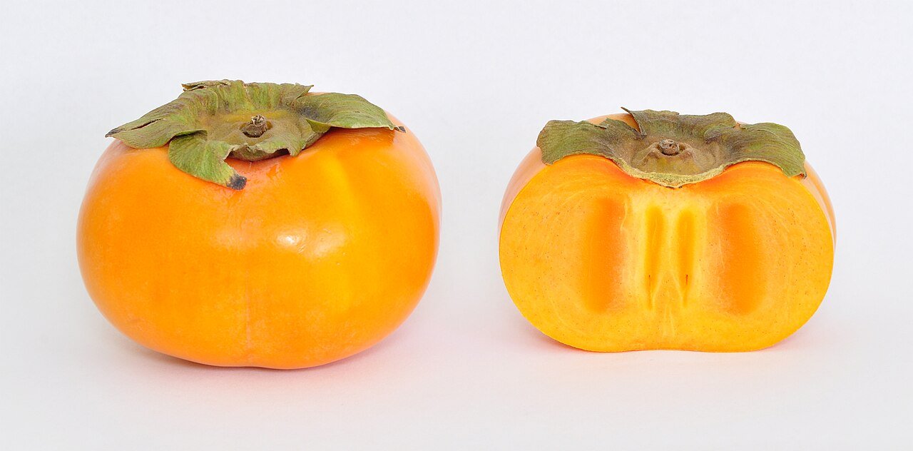 Caqui Fuyu inteiro e cortado ao meio, com o talo verde